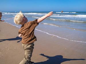 布洛克胡斯4 person holiday home on a holiday park in Blokhus的一名男孩在沙滩上扔飞盘