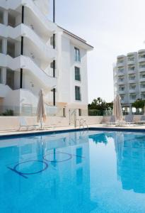 圣安东尼奥湾BA Style Apartments Ibiza的大楼前的游泳池配有椅子和遮阳伞