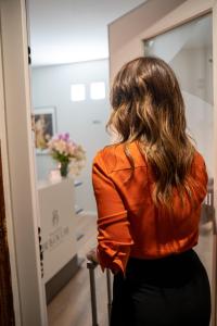 布林迪西Palazzo Bellocchi - Suites & Apartments的穿着橙色衬衫的女人,看着镜子