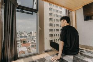岘港IKIGAI Dorm Hostel - Danang Centre的坐在地板上,望着窗外的人