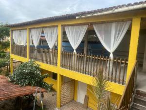 伊塔乌纳斯POUSADA DO SOL ITAUNAS的黄色房子,阳台配有白色窗帘