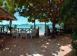 爱妮岛Corong Beach Resort的海滩上树下的桌椅
