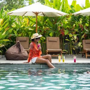 塞隆贝拉纳克Bruga Villas Restaurant and Spa的坐在游泳池旁的戴帽子的女人