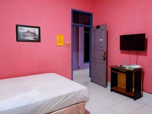 BaubauHotel Rosichan Bau Bau Mitra RedDoorz的卧室设有粉红色的墙壁、一张床和一台电视机