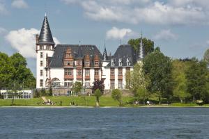 克林克Seehotel Schloss Klink的一座白色的大建筑,有黑色的屋顶,靠近水体