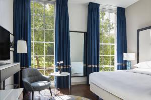 伦敦万豪伦敦格罗夫纳广场酒店的一间卧室配有蓝色窗帘、一张床和椅子