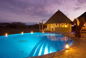 Tsavo West National ParkSeverin Safari Camp的一座大型游泳池,在晚上在房子前面