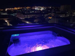 卡利亚里18 Dante Luxury Suites的紫色浴缸,晚上可欣赏到城市美景