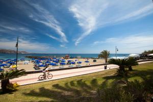美洲海滩Optimist Tenerife的一片带蓝色遮阳伞的海滩,还有一位骑自行车的人