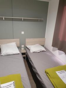 纳博讷普拉日Mobil home - Clim, TV - Camping '4 étoiles' - Narbonne Plage - 014的小客房内的两张床,配有白色床单和黄色毯子