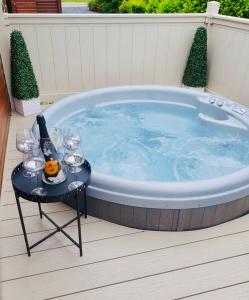 莫尔顿Green Acres Retreat Lodge with Hot Tub的按摩浴缸,配有带酒杯和一瓶酒的桌子