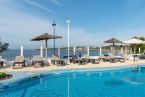 萨尔加AluaSun Far Menorca的毗邻大海的带椅子和遮阳伞的游泳池