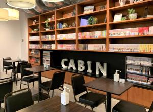 东京First Cabin Ichigaya的图书馆配有桌椅和书架