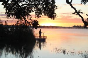 利文斯顿Kayube Zambezi River House的日落时分在湖面上钓鱼的男人