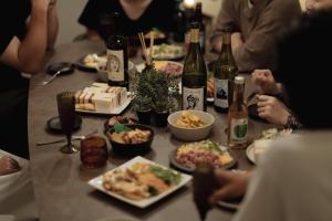 金泽Good Neighbors的一群人坐在桌子旁,一边吃着食物和葡萄酒