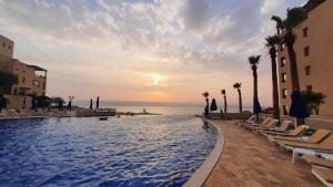 索瓦马Comfy Stays Sea View Apartments at DeadSea Samarah Resort的一个带椅子的游泳池,日落时分享有海景