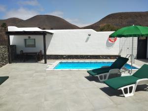 MáguezFinca La Tabaiba Apartamento alto的一个带两把椅子和遮阳伞的游泳池