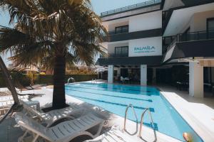 锡利夫凯PALMİLA BUTİK OTEL的一座带椅子的游泳池,一座建筑前的棕榈树