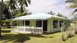 拉罗汤加Flame Cottage的绿色房子,拥有白色门廊和棕榈树
