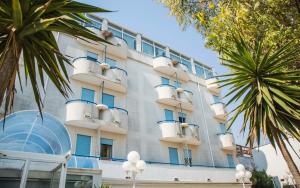 托雷坎内Eden Beach Club的一座白色的大建筑,拥有蓝色的窗户和棕榈树