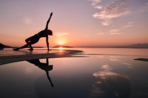 伊罗达Elounda Gulf Villas by Sandglass的日落时在海滩上做瑜伽姿势的女人