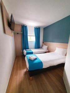 希利马扎兰Kyriad Direct Chilly-Mazarin的小房间设有两张床,配有蓝色窗帘