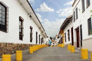 卡利HOSTAL CHONTADURO Casa colonial en pleno centro histórico de Cali- Se alquila la casa entera para 12 o 13 personas o por habitaciones的一条有白色建筑和黄色柱子的小巷