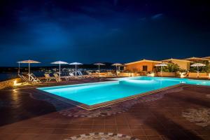 阿兰奇湾城Appartamenti Marineledda Golfo di Marinella的夜间游泳池,配有椅子和遮阳伞