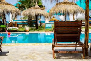 迈来亚Hotel de charme et SPA Dar El Bhar的一把椅子,坐在一个带稻草遮阳伞的游泳池边