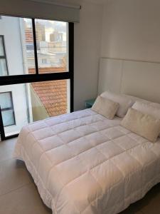 马德普拉塔departamento San Carlos的一张大白色的床,位于一个设有大窗户的房间