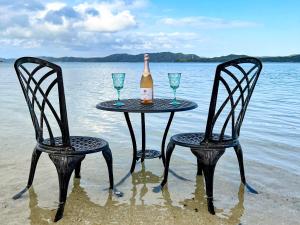 奄美Le Grand Bleu的沙滩上的两把椅子和一张桌子,上面放着一瓶酒和酒杯