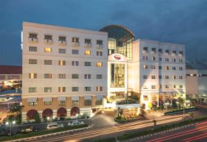 泗水Surabaya Suites Hotel Powered by Archipelago的一座白色的大建筑,前面有汽车停放