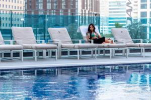 迪拜Unlock Metropolis Business Bay的坐在游泳池旁椅子上的女人