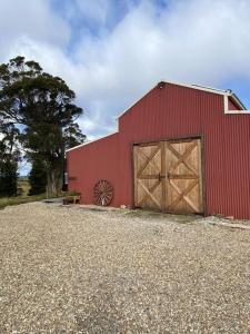 Joadja CreekFarm Stay Unique Barn in Southern Highlands的红谷仓,有两扇木门和一棵树