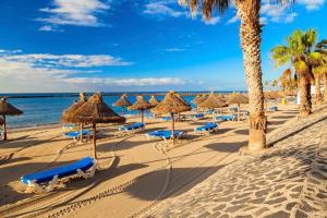 洛斯克里斯蒂亚诺斯Luminoso y bonito apartamento con piscina en frente del mar的一个带草伞和椅子的海滩和大海