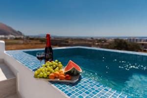 佩里萨The Tree Houses Santorini的游泳池旁的水果盘和一瓶葡萄酒