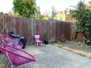 伦敦A lovely guest room in West London的庭院设有两把粉红色的椅子和围栏