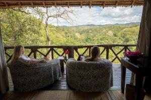 KisakiSable Mountain Lodge, A Tent with a View Safaris的两个女孩坐在门廊的椅子上,享有美景