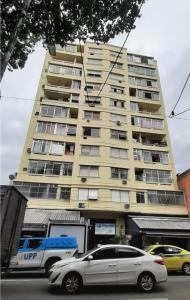 里约热内卢Sweet Studio Lapa的一座高大的黄色建筑,前面有汽车停放