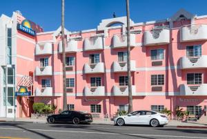 洛杉矶Days Inn by Wyndham Santa Monica的两辆汽车停在粉红色建筑前