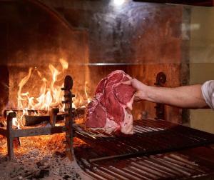 丘西Hotel Villa Il Patriarca的男人把一块肉放在烤架上