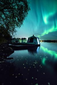 罗瓦涅米Aurora Nest – Eco Glass Igloo的一艘船坐在水面的北极光下