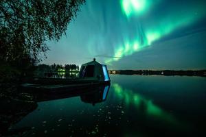 罗瓦涅米Aurora Nest – Eco Glass Igloo的一艘船坐在极光下的水面上