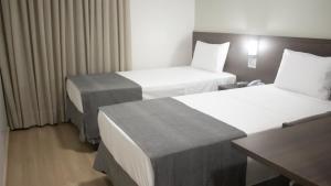 弗朗西斯科贝尔特朗Essência Hotel Francisco Beltrão的酒店客房设有两张床和一张桌子。