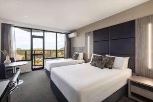 阿德莱德Rydges South Park Adelaide的酒店客房设有两张床、一张书桌和一个窗户。