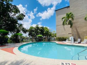 肯代尔The Palms Inn & Suites Miami, Kendall, FL的一座带椅子和遮阳伞的游泳池位于一座建筑旁边