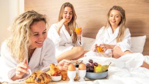 奈梅亨Sanadome Hotel & Spa Nijmegen的三个坐在床上吃食物和喝果汁的女人