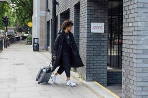 伦敦YOTEL London Shoreditch的带着手提箱沿着人行道走的女人