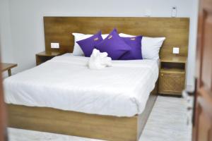 恩德培Tenda Suites and Restaurant的一只白色填充动物坐在床上,床上有紫色枕头