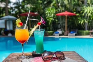 华欣华欣拉萨苏巴度假酒店的坐在泳池旁的桌子上,喝上两杯鸡尾酒